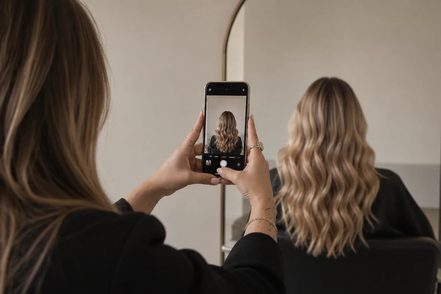A hairstylist photographing the back of a client's wavy blonde hair